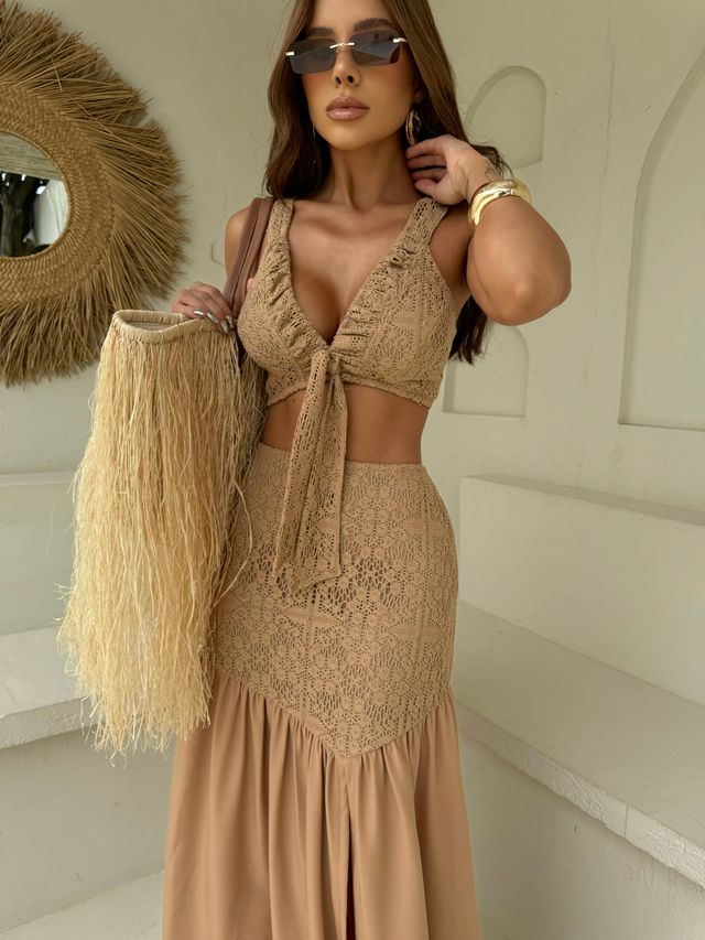 Modelo usando conjunto bege de cropped com amarração frontal e saia longa de crochê segurando bolsa de palha