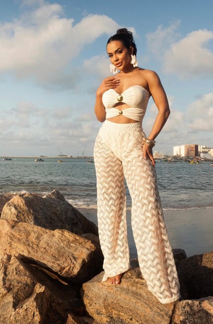 Close-up de modelo usando conjunto off-white de top tomara que caia com detalhes dourados e calça de crochê