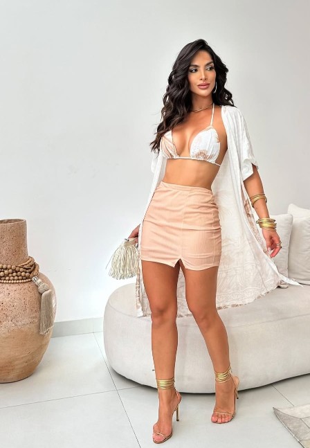 Modelo em ambiente elegante usando quimono branco com estampa de folhagens sobre top de biquíni e saia curta bege