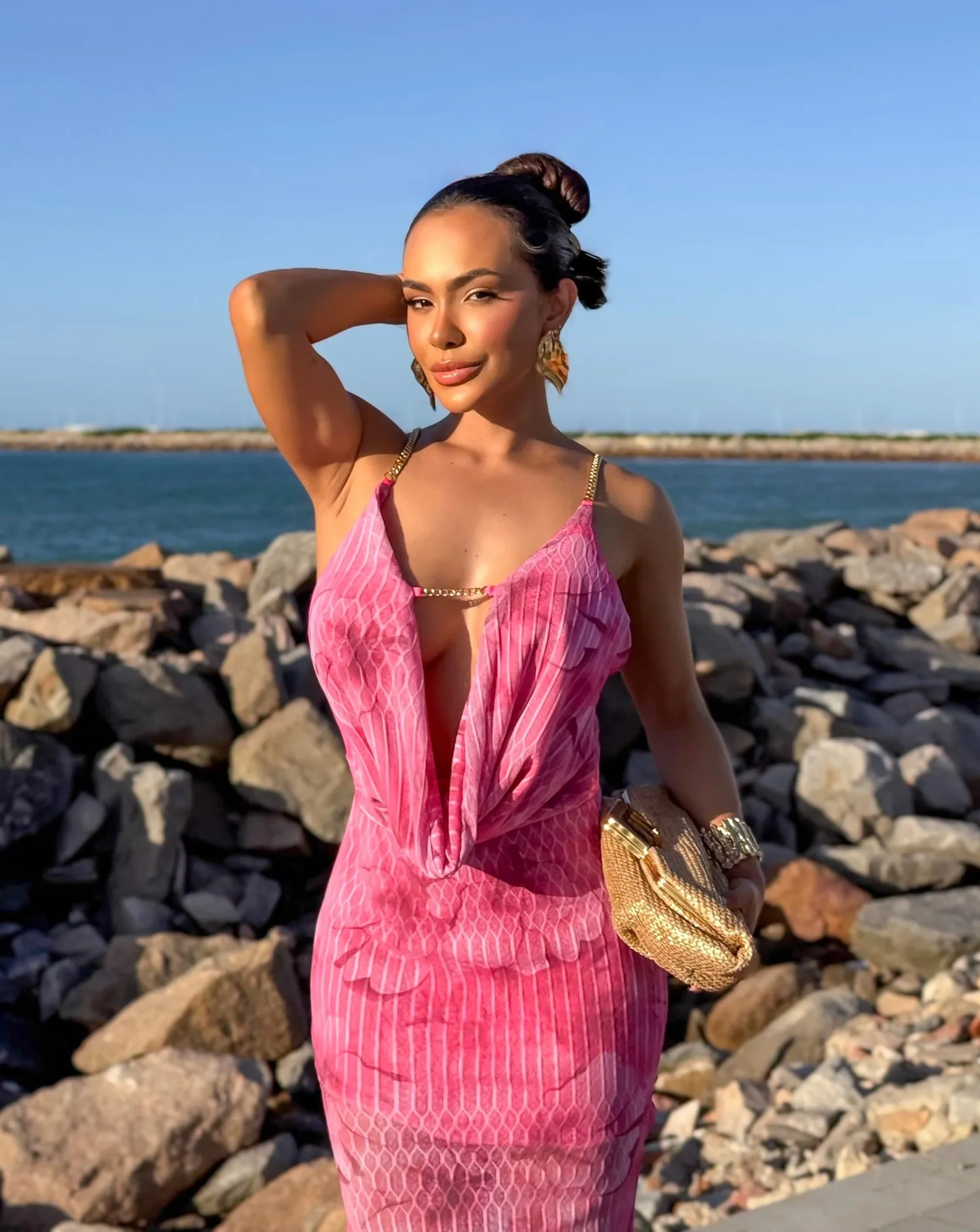 Modelo usando vestido longo rosa plissado com decote cascata e corrente dourada